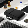 A black laptop bag is displayed on a white and black striped surface, surrounded by various materials like foam, beads, and spools of thread. Produktbild-Vorschau