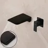 A black wall-mounted faucet with a waterfall spout and a separate control handle, mounted on a beige tiled wall. Náhled obrázku produktu