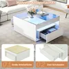 A modern white coffee table with glass top and LED lighting, shown in a living room setting with a sofa. Voir les images du produit