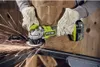 A person wearing gloves and an apron is using a Ryobi angle grinder to cut metal, with sparks flying. Produktbild-Vorschau