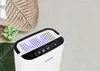 A white dehumidifier with a digital display sits on a textured surface, next to decorative items. Náhľad obrázku produktu