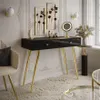 A modern vanity table with gold legs and drawers, decorated with wall art and a mirror, in a well-lit room. Náhled obrázku produktu