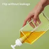 A hand is holding a clear plastic bottle with yellow liquid, pouring it out. Produktbild-Vorschau