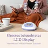 A person is using a breast pump while sitting on a couch, with a cup and a book on a table in the foreground. Produktbild-Vorschau