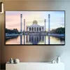 A large flat-screen television displaying a mosque and its reflection in water, mounted on a wall above a white cabinet with decorative items. Náhľad obrázku produktu
