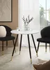 A round marble-look dining table with black and gold legs, set between two black chairs in a well-lit room with sheer curtains. Produktbild-Vorschau