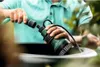 A person is connecting a green hose to a green and black submersible pump unit that is being lowered into a large gray container. Náhľad obrázku produktu