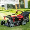 A red and black lawnmower is shown on a green lawn in front of a blurred background of a house and trees. Produktbild-Vorschau