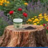 A container of garden product and a pile of granules are placed on a tree stump in front of a blurred garden with flowers. Produktbild-Vorschau