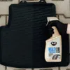 A hand in a black glove is holding a bottle of K2 BOLD Tyre Care product over a black car mat. Podgląd zdjęcia produktu