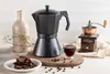 A still life arrangement featuring a moka pot, a coffee grinder, a cup of coffee, and cookies. Náhľad obrázku produktu