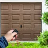 A hand holding a remote control in front of a garage door. Voir les images du produit