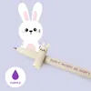 A cartoon bunny illustration is shown behind a cream-colored pen with purple text. Produktbild-Vorschau