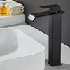 A black waterfall faucet is shown next to a white sink, with a bottle of liquid and a folded towel in the background. Produktbild-Vorschau