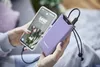 A person is holding a smartphone and a purple power bank, with the power bank charging the phone. Voir les images du produit