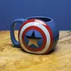 A blue mug designed to look like Captain America's shield sits on a wooden table against a blue background. Produktbild-Vorschau