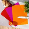 A set of three flexible cutting boards in red, magenta, and orange, with a loaf of bread, an apple, and a knife. Voir les images du produit
