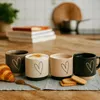 Four ceramic mugs with heart designs are arranged on a table with a croissant and cookies. Náhled obrázku produktu