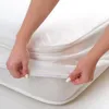 Hands are shown putting a white mattress protector onto a mattress. Produktbild-Vorschau