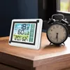 A digital weather station and an alarm clock are placed on a wooden table next to a window. Náhled obrázku produktu