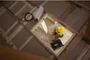 A construction worker is measuring a space in what appears to be an attic or unfinished room. Voir les images du produit