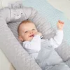 A baby is lying in a grey baby lounger with a bear face design, on a light blue quilted mat. Anteprima dell’immagine prodotto
