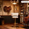 A vintage-style barber shop interior with a saddle on the wall, a barber chair, and a bar stool. Produktbild-Vorschau