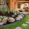 A garden scene with a flower bed bordered by a rattan-look plastic edging, leading to a patio with outdoor furniture and a grill. Náhled obrázku produktu