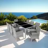 A rattan dining set with a black tabletop is placed on a patio overlooking the ocean and a swimming pool. Voir les images du produit