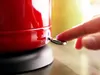 A close-up of a red electric kettle being switched on. Produktbild-Vorschau
