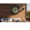 A large, illuminated outdoor clock with thermometer and hygrometer mounted on a wooden wall above a sofa with cushions. Produktbild-Vorschau