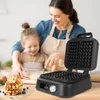A mother and daughter are in a kitchen, preparing waffles. The waffle maker is in the foreground, with a stack of waffles next to it. Náhľad obrázku produktu