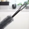 A close-up of a cleaning brush with a black handle and gray bristles, set against a blurred background of a room with a window. Podgląd zdjęcia produktu