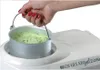 A hand is holding a container of green ice cream over an ice cream maker. Voir les images du produit