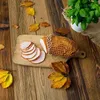 A smoked meat product, sliced and whole, on a wooden cutting board, surrounded by autumn leaves on a wooden table. A pot of basil is visible in the background. Produktbild-Vorschau