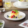 A dessert with berries and kiwi on a white plate, with a glass of water and a bowl of spices in the background. Náhled obrázku produktu