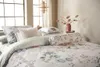 A beautifully made bed with floral patterned bedding, pillows, and a bolster pillow, set against a window with natural light. Produktbild-Vorschau