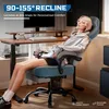 A woman is relaxing in a gaming chair in front of a desk. Produktbild-Vorschau