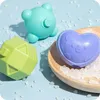 Three colorful baby toys are arranged on a light blue background with small white beads scattered around. Produktbild-Vorschau