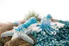A collection of stuffed sea creatures arranged on a white surface with a fishing net and blue confetti. Produktbild-Vorschau