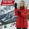 A woman wearing a red winter jacket and black gloves stands in a snowy mountain landscape. Produktbild-Vorschau
