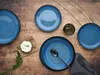 A table setting with blue ceramic plates, a small appetizer, and a napkin. Náhľad obrázku produktu