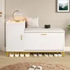 A white shoe cabinet with a padded seat and gold accents, placed in a room with a rug and a framed picture on the wall. Produktbild-Vorschau