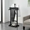 A black valet stand with a white shirt, gray pants, and gray shoes on it, placed in a room with a gray armchair and a plant. Produktbild-Vorschau