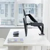 A dual monitor stand is mounted on a desk in front of a window. Náhled obrázku produktu