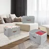 Several fabric storage boxes are arranged in a living room setting, with one box open and containing a red book. Podgląd zdjęcia produktu