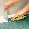 A person is using a utility knife to cut carpet near a wall. Produktbild-Vorschau