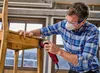 A man is sanding a wooden chair with a power tool. Náhľad obrázku produktu