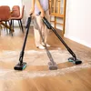 A person is using two cordless stick vacuums to clean up white powder from a wooden floor in a room with furniture. Náhled obrázku produktu