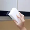 A hand is holding a white cleaning sponge and wiping a dark surface. Produktbild-Vorschau